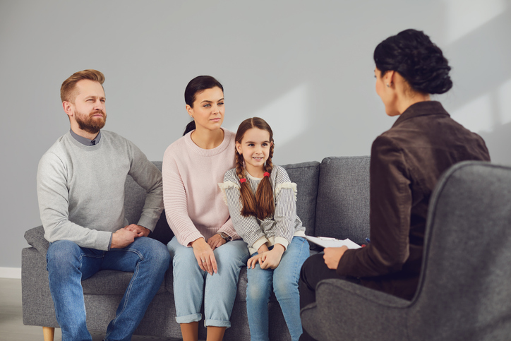 Familienberatung. Beraterin und Ehepaar mit einem Kind sitzen auf der Couch